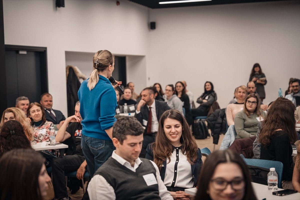 A participant asking a question with a microphone among her seated colleagues